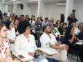 Fotografia de cerca de 80 participantes da formação do CREPOP sentados em carteiras em um auditório. No primeiro plano, da esquerda para a direita, estão sentados o conselheiro do CFP Leandro Amorim Rosa, a conselheira do CFP Miriam Alves e o supervisor do CREPOP Bruno Correia da Mota.